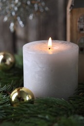 Photo of Burning candle, baubles and fir branches on blurred background, closeup. Christmas atmosphere