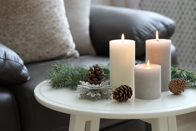 Photo of Burning candles, fir branches and other Christmas decor on coffee table indoors