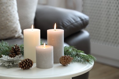 Photo of Burning candles, fir branches and other Christmas decor on coffee table indoors