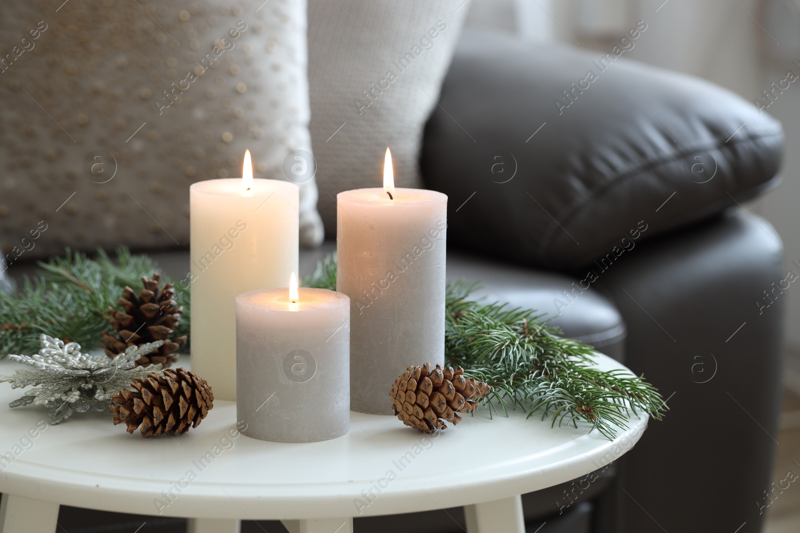 Photo of Burning candles, fir branches and other Christmas decor on coffee table indoors