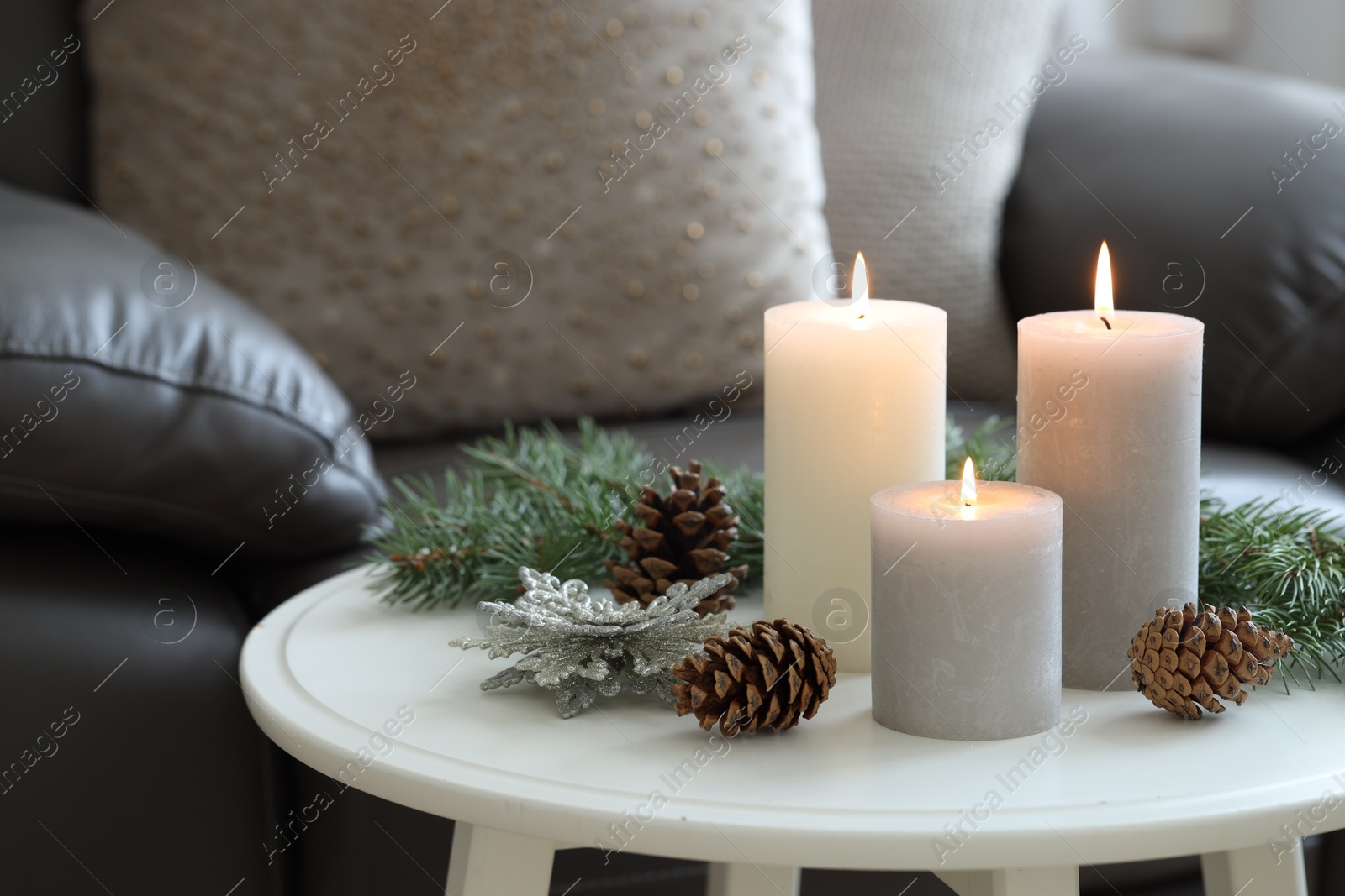 Photo of Burning candles, fir branches and other Christmas decor on coffee table indoors