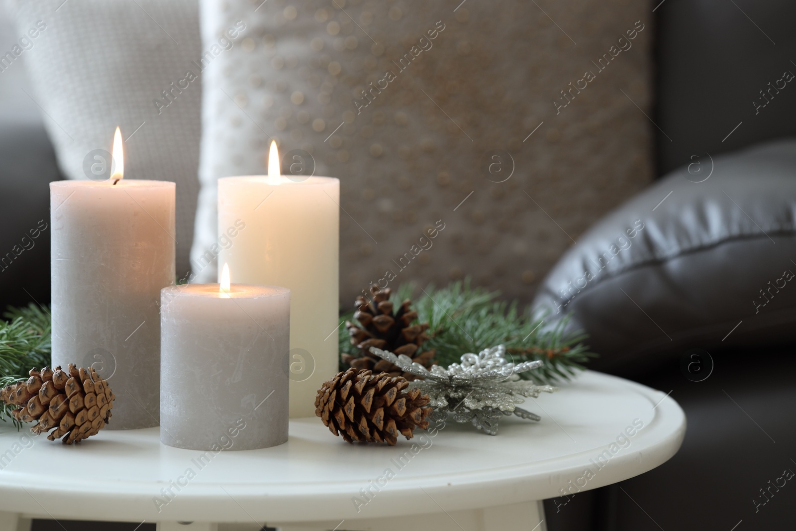 Photo of Burning candles, fir branches and other Christmas decor on coffee table indoors