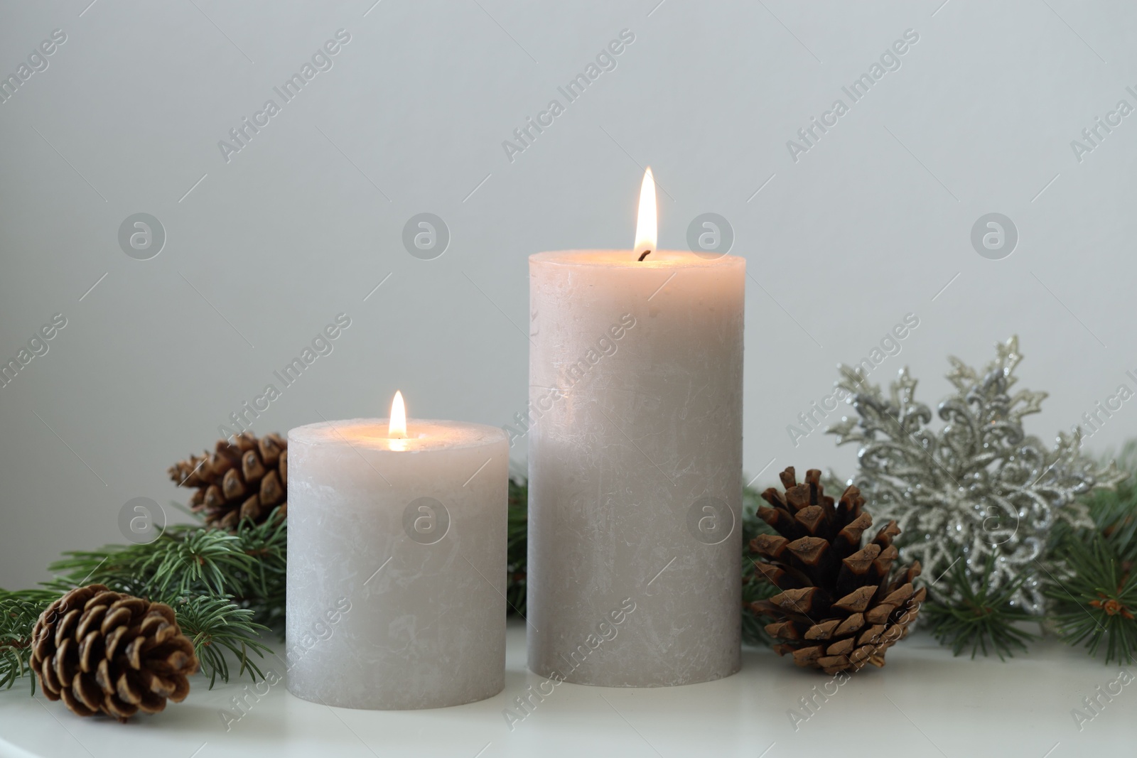 Photo of Burning candles and fir branches on white table. Christmas atmosphere