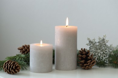 Photo of Burning candles and fir branches on white table. Christmas atmosphere