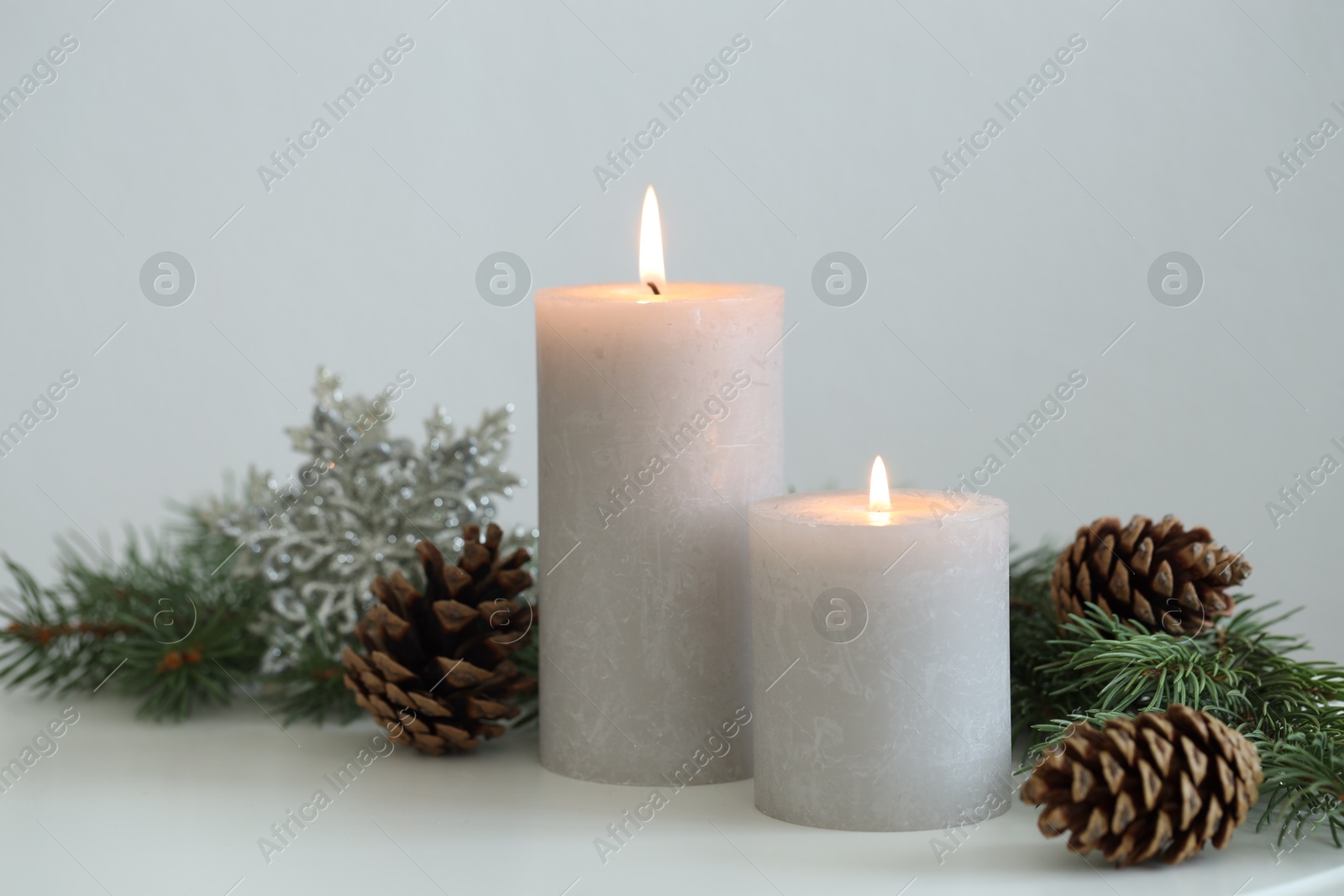 Photo of Burning candles and fir branches on white table. Christmas atmosphere