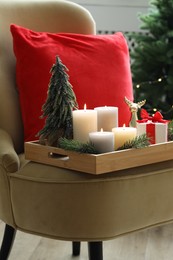 Photo of Tray with burning candles and Christmas decor on armchair indoors