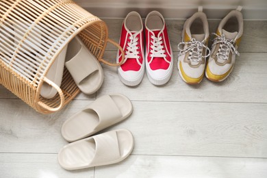 Photo of Basket with slippers for guests and sneakers in entryway at home, above view