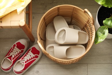 Photo of Basket with slippers for guests and sneakers in entryway at home, above view