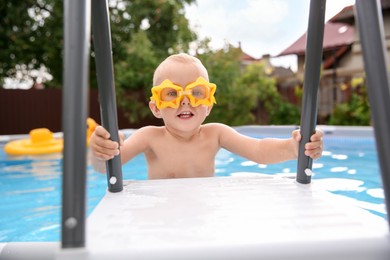 Photo of Little boy getting out of swimming pool by ladder outdoors