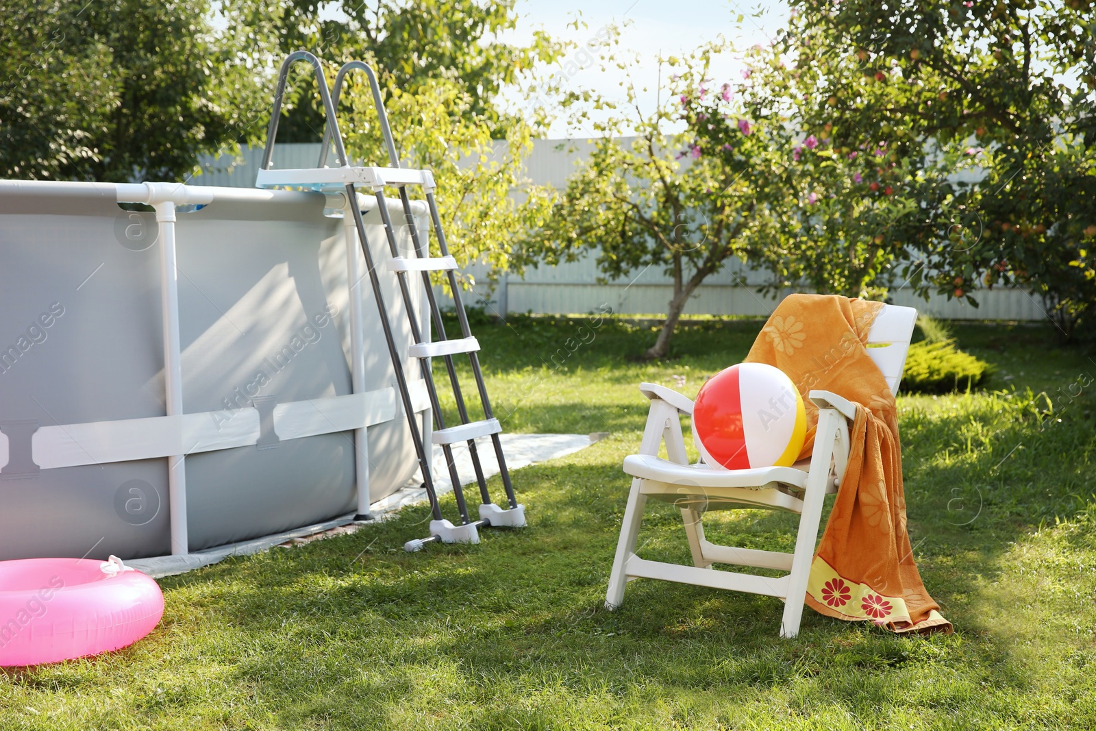 Photo of Above ground swimming pool, folding chair, towel, inflatable ring and ball in backyard