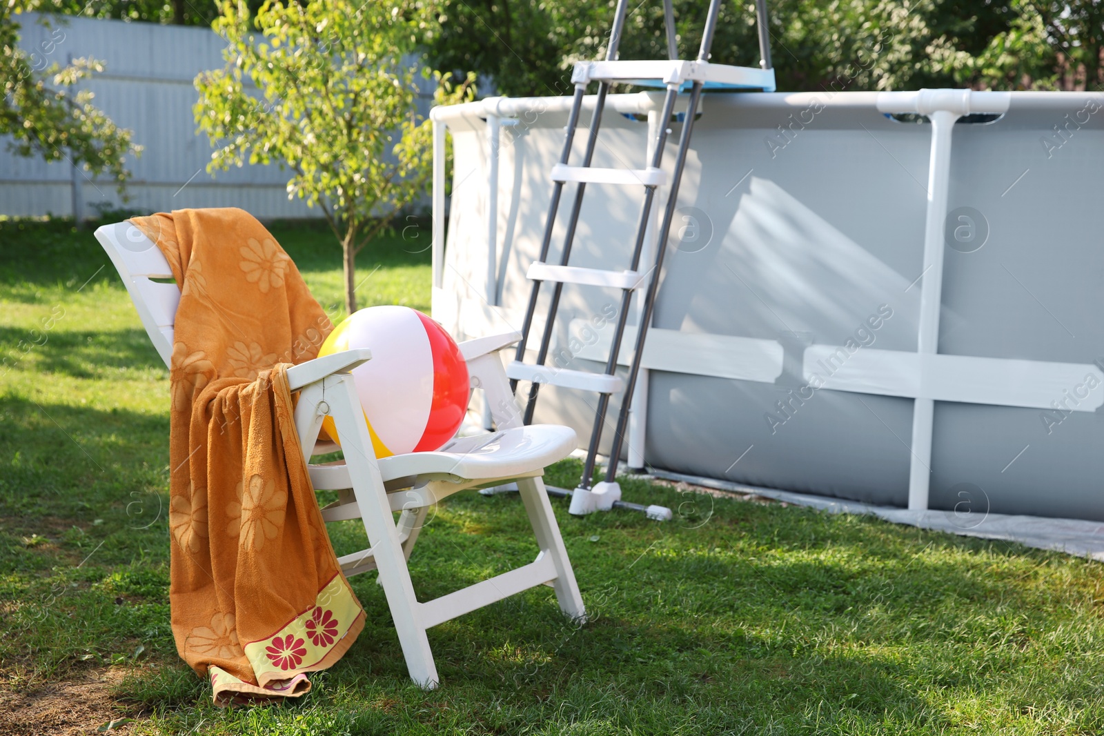 Photo of Above ground swimming pool, folding chair, towel, inflatable ring and ball in backyard