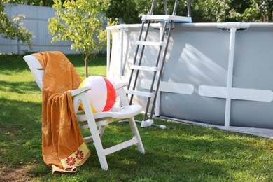 Photo of Above ground swimming pool, folding chair, towel, inflatable ring and ball in backyard