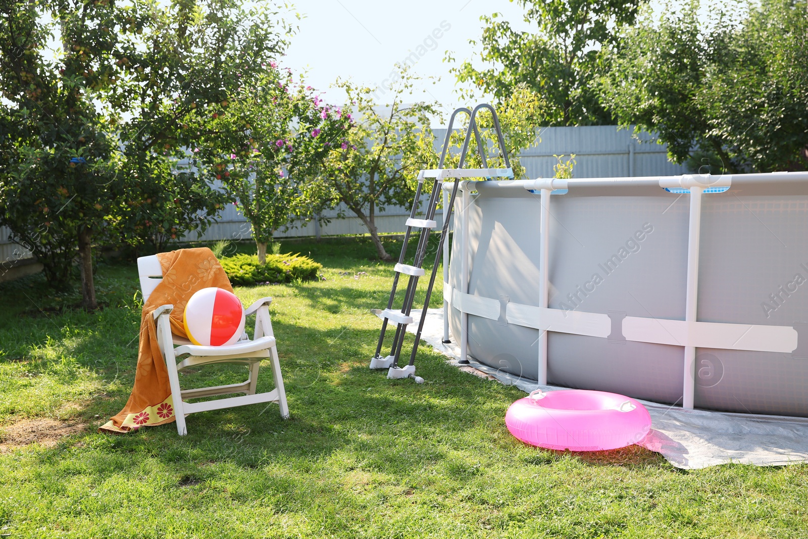 Photo of Above ground swimming pool, folding chair, towel, inflatable ring and ball in backyard