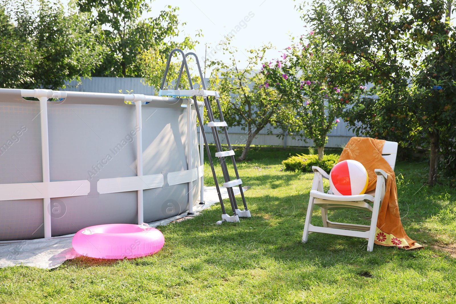 Photo of Above ground swimming pool, folding chair, towel, inflatable ring and ball in backyard