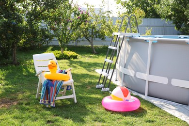 Photo of Above ground swimming pool, folding chair, towel, inflatable rings and ball in backyard