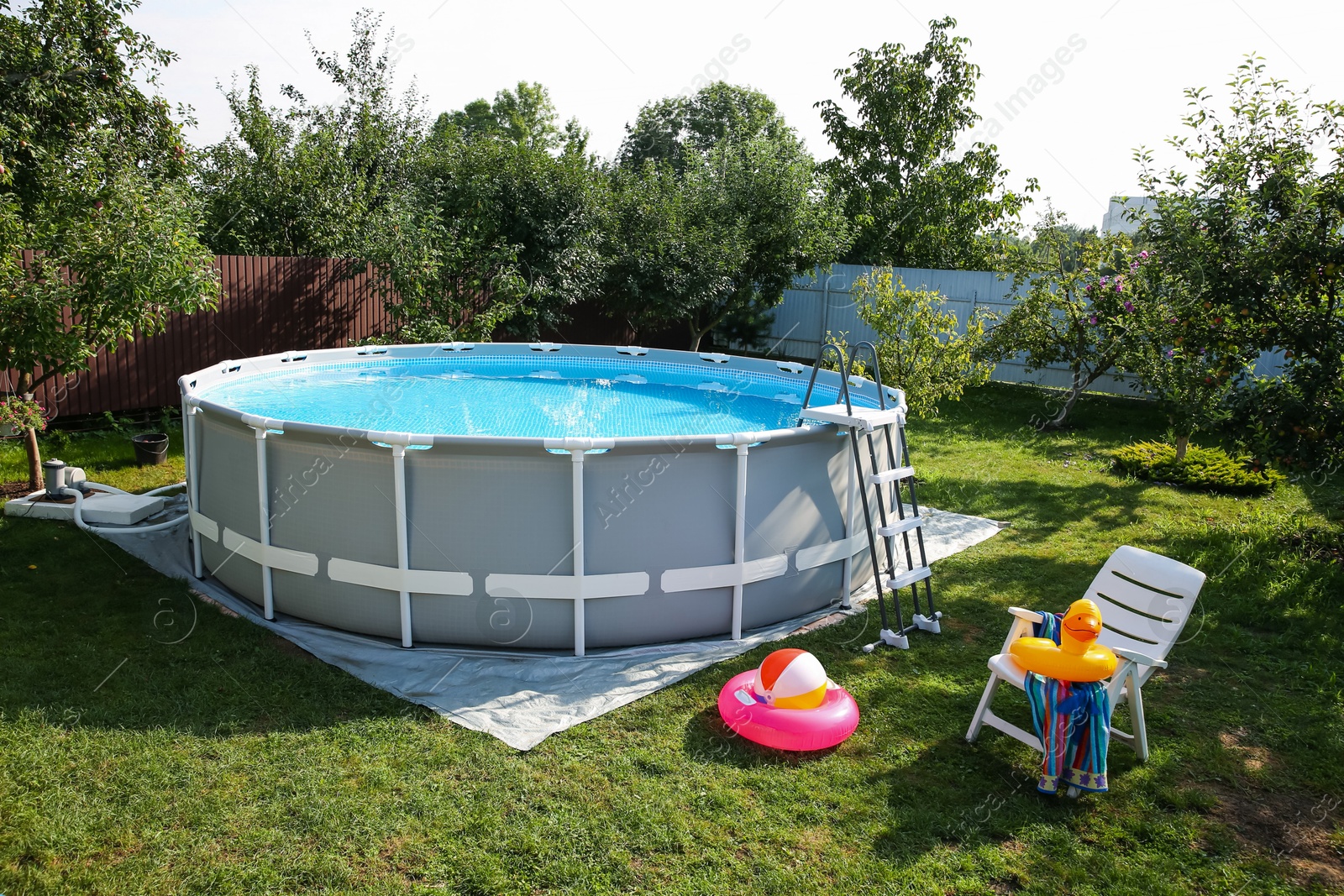 Photo of Above ground swimming pool, folding chair, towel, inflatable rings and ball in backyard