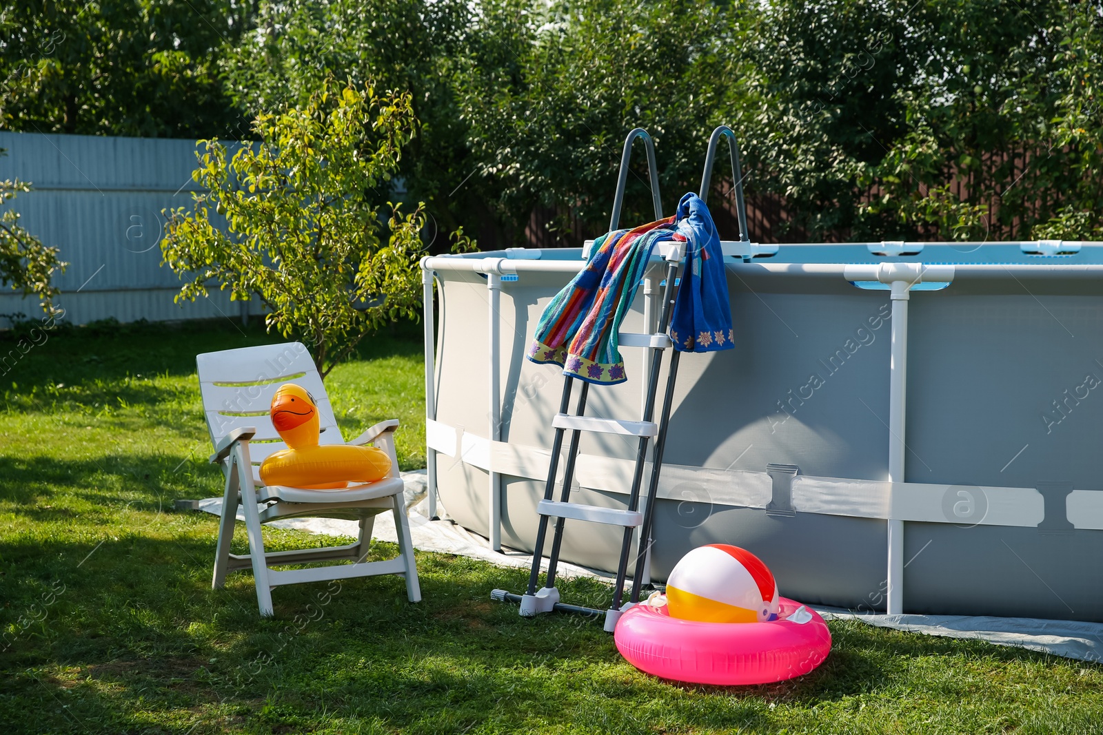 Photo of Above ground swimming pool, folding chair, towel, inflatable rings and ball in backyard