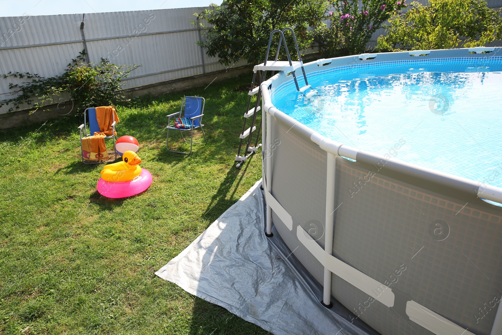 Photo of Above ground swimming pool, folding chairs, towel, inflatable rings and ball in backyard