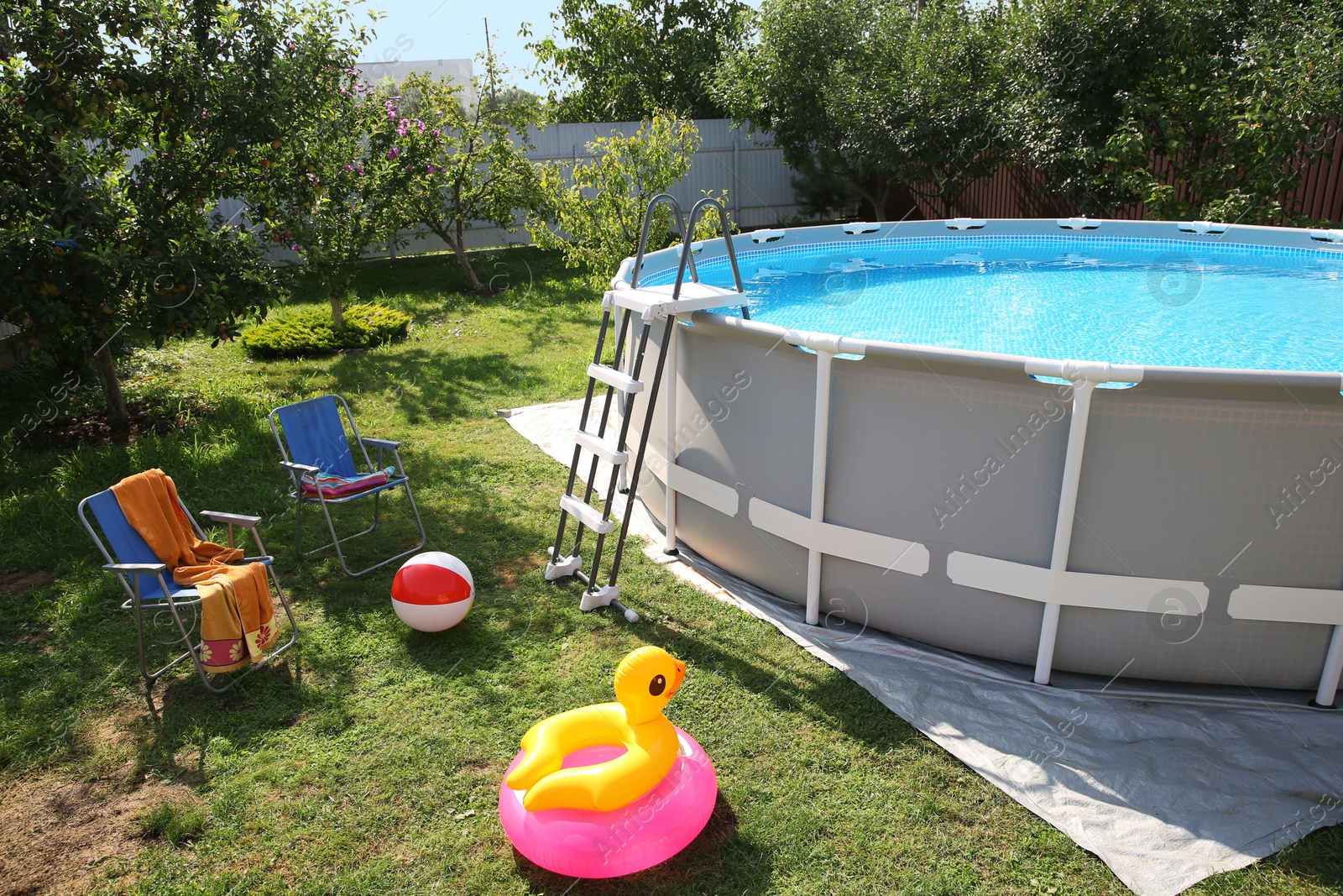 Photo of Above ground swimming pool, folding chairs, towel, inflatable rings and ball in backyard