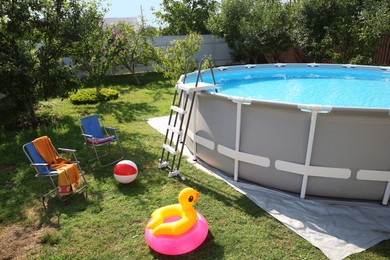 Above ground swimming pool, folding chairs, towel, inflatable rings and ball in backyard