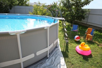 Above ground swimming pool, folding chairs, towel, inflatable rings and ball in backyard