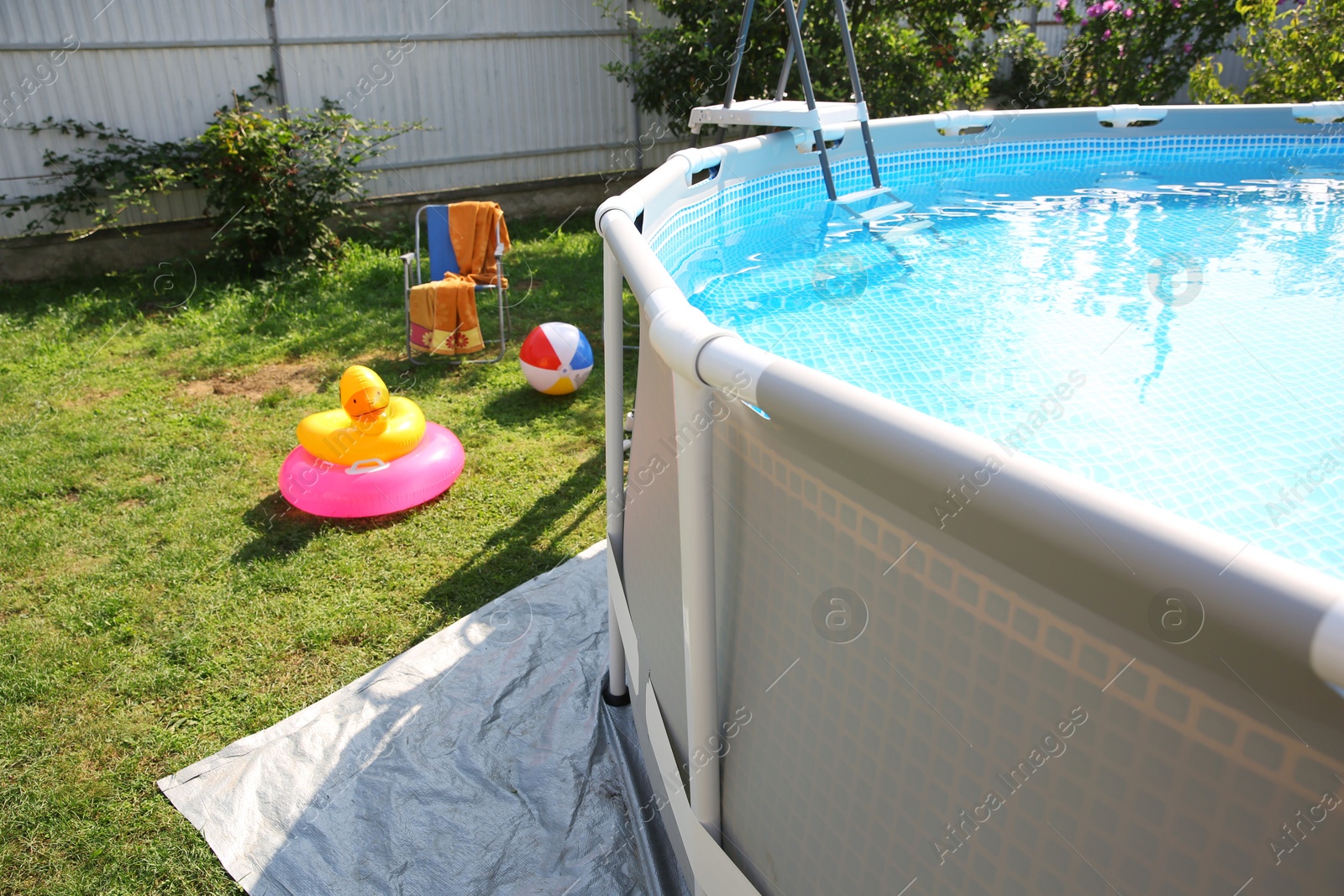 Photo of Above ground swimming pool, folding chairs, towel, inflatable rings and ball in backyard