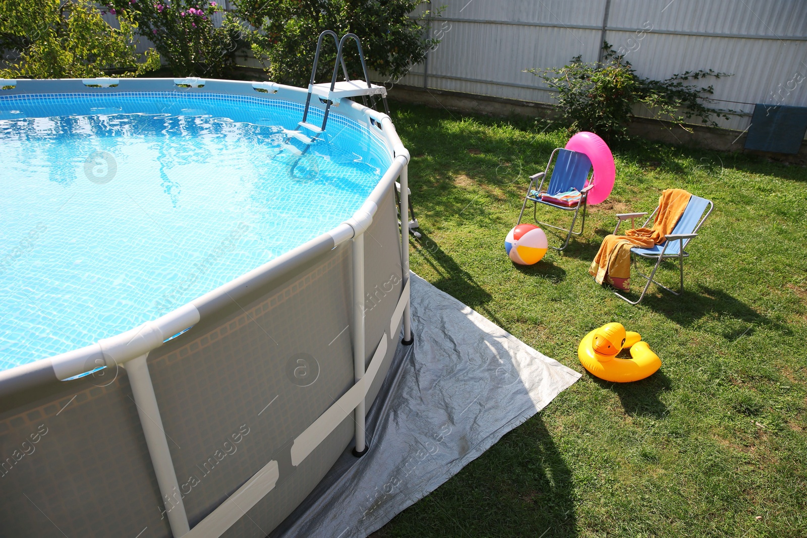 Photo of Above ground swimming pool, folding chairs, towel, inflatable rings and ball in backyard