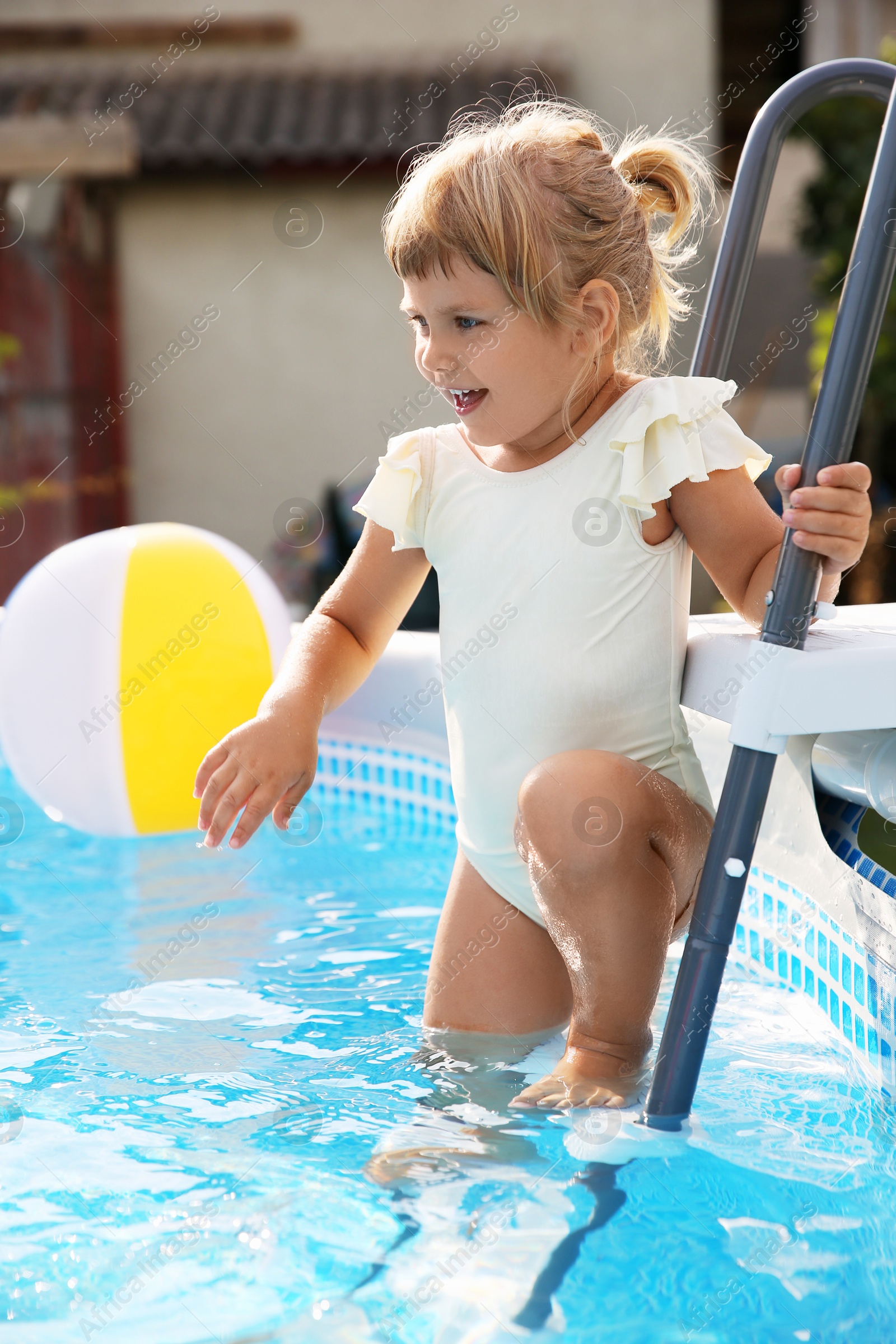 Photo of Little girl on ladder in swimming pool outdoors