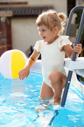 Little girl on ladder in swimming pool outdoors