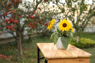 Photo of Vase with sunflowers on wooden table in garden