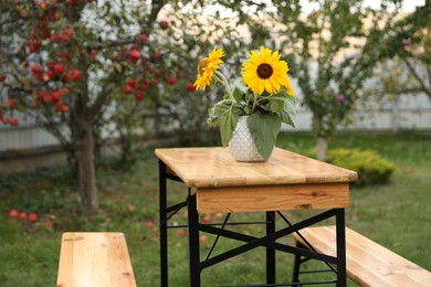 Vase with sunflowers on wooden table in garden