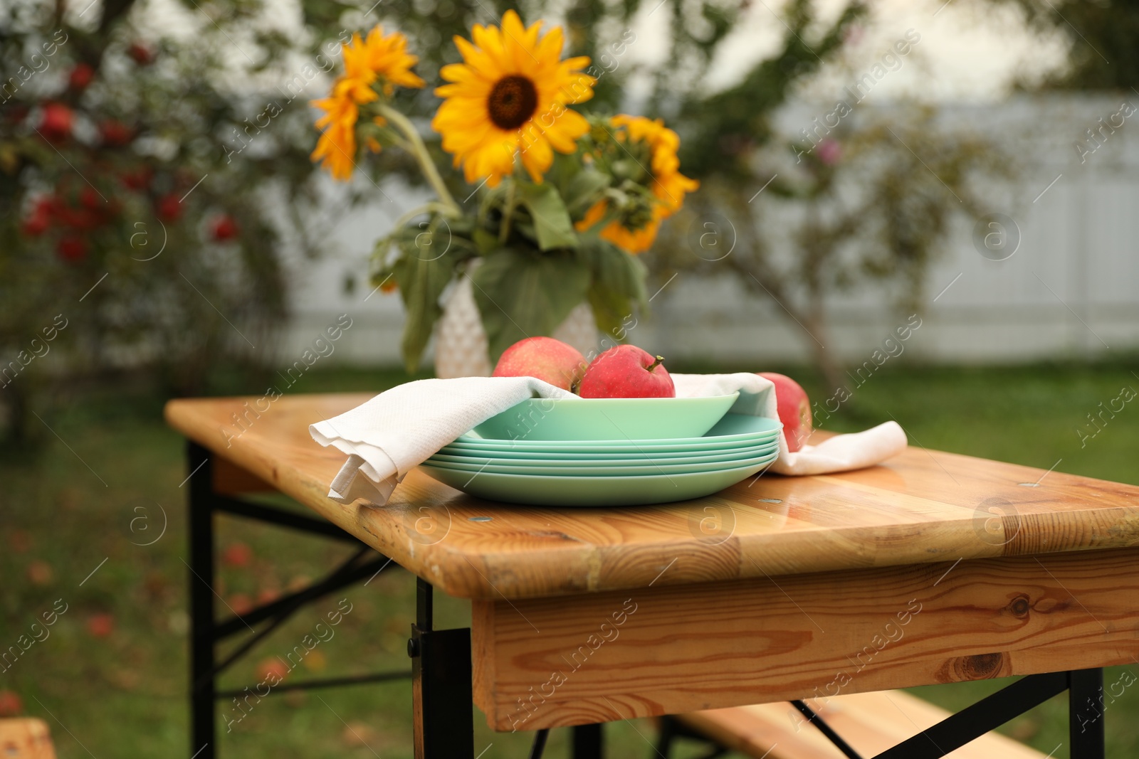 Photo of Apples and vase with sunflowers on wooden table in garden, selective focus