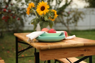 Photo of Apples and vase with sunflowers on wooden table in garden, selective focus