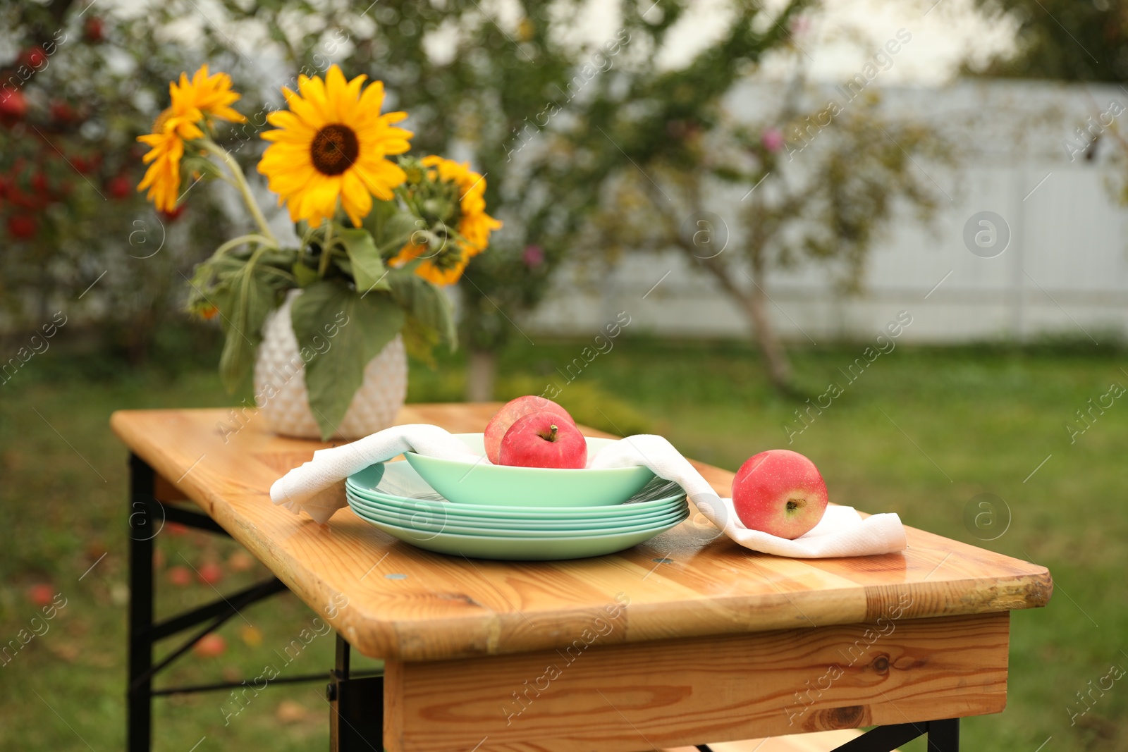 Photo of Apples and vase with sunflowers on wooden table in garden, selective focus