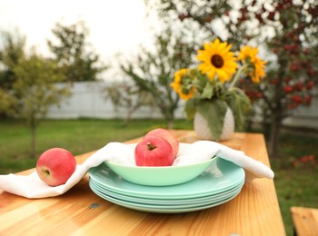 Photo of Apples and vase with sunflowers on wooden table in garden, selective focus