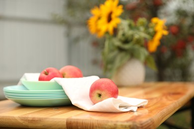 Photo of Apples and vase with sunflowers on wooden table in garden, selective focus