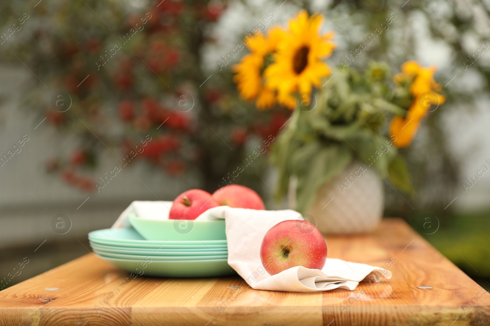 Photo of Apples and vase with sunflowers on wooden table in garden, selective focus