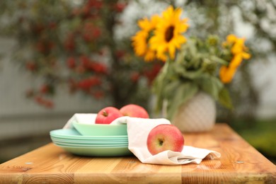 Photo of Apples and vase with sunflowers on wooden table in garden, selective focus