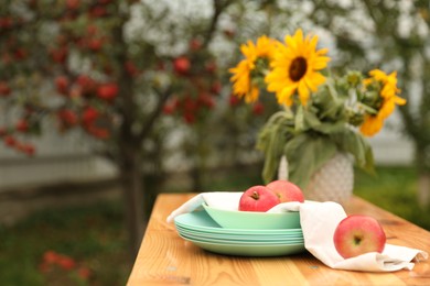 Apples and vase with sunflowers on wooden table in garden, selective focus