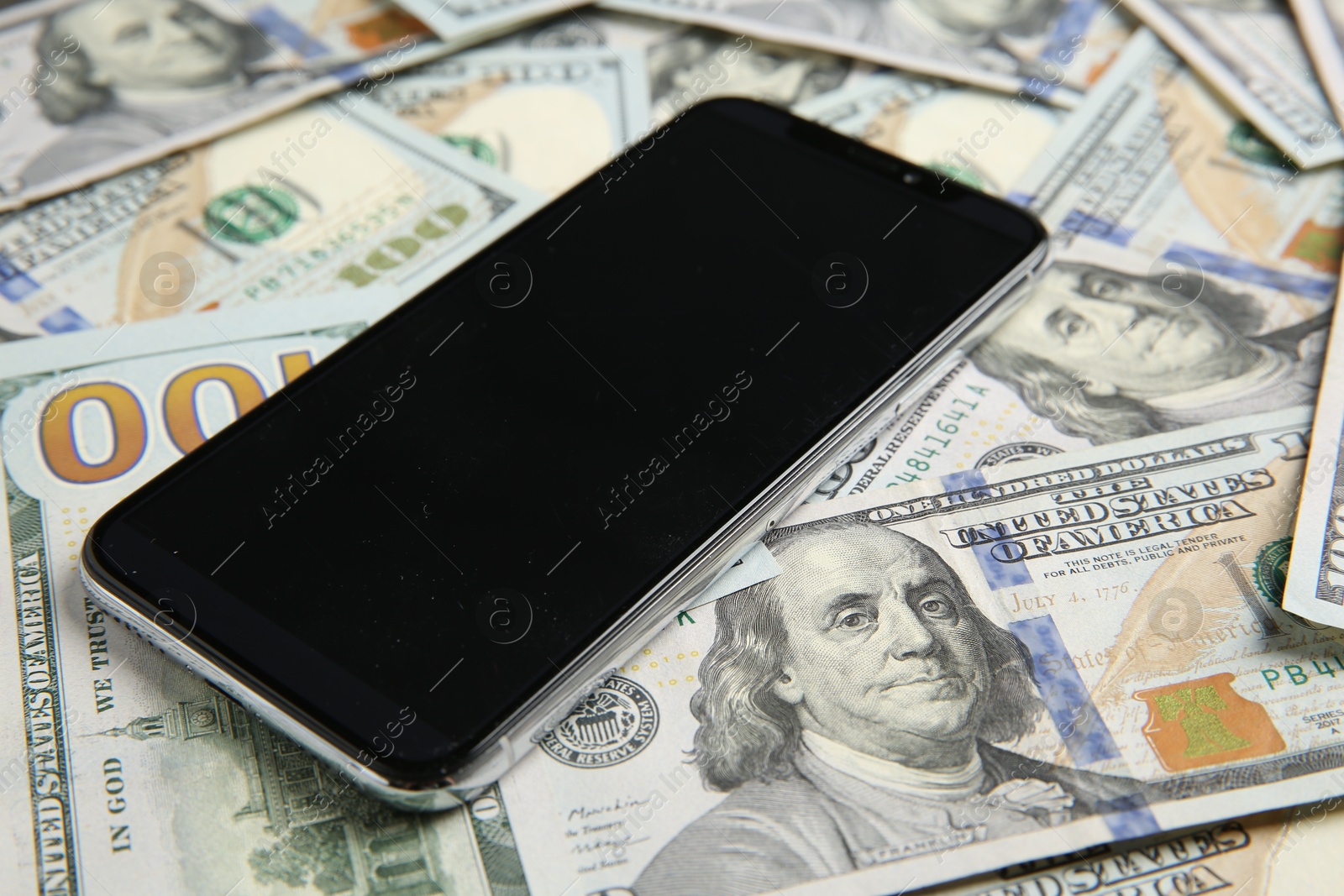 Photo of Modern smartphone on dollar bills, closeup view