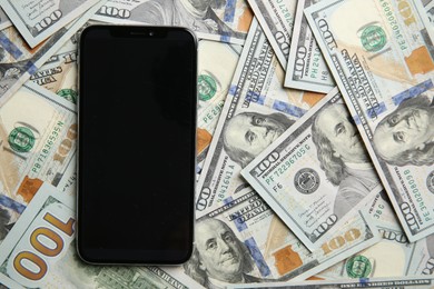 Photo of Modern smartphone on dollar bills, top view