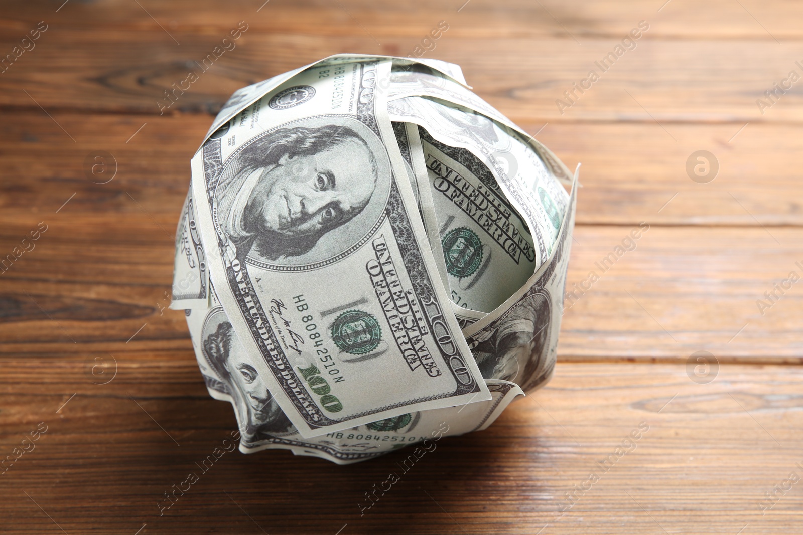 Photo of Ball made of dollars on wooden table, closeup