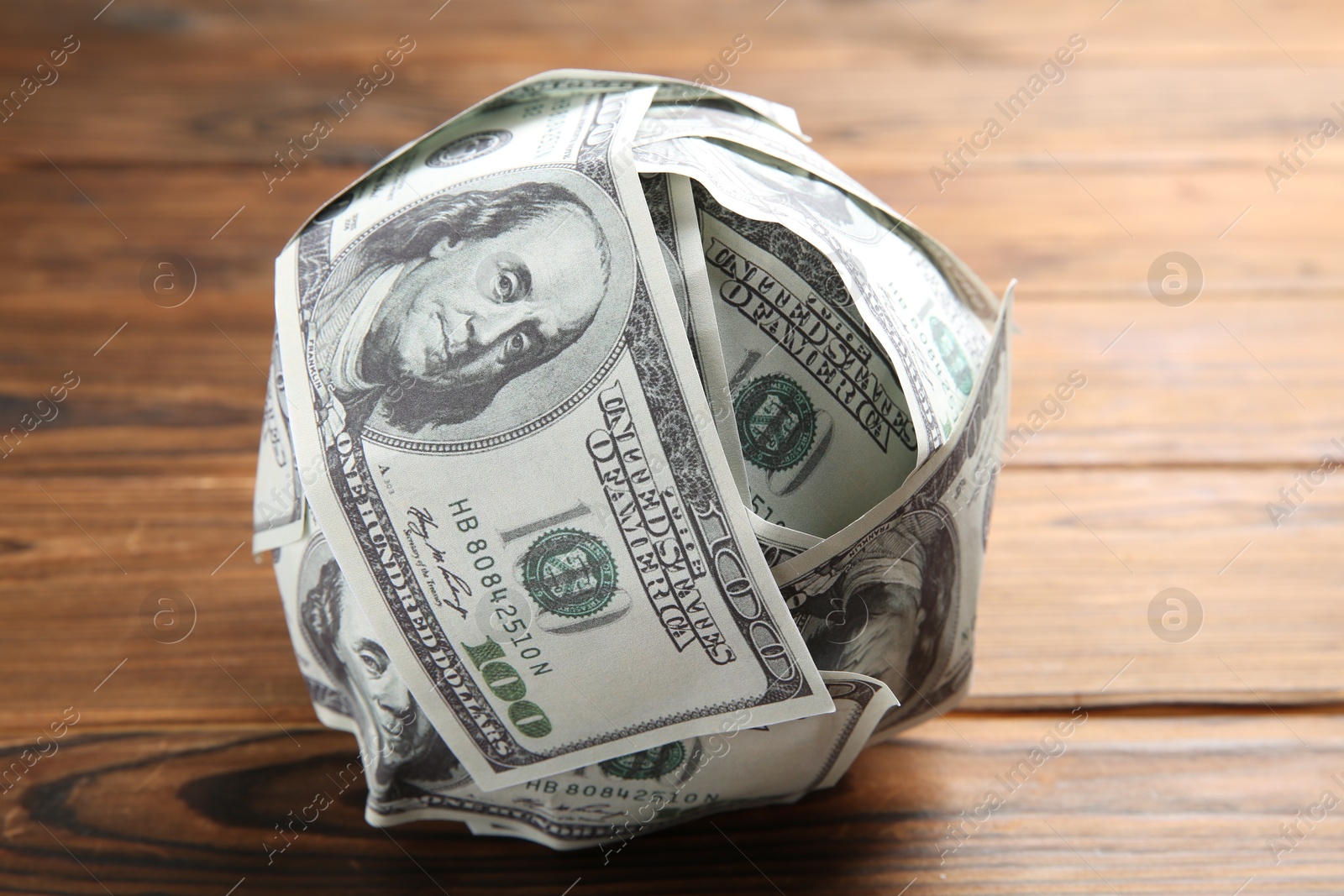 Photo of Ball made of dollars on wooden table, closeup