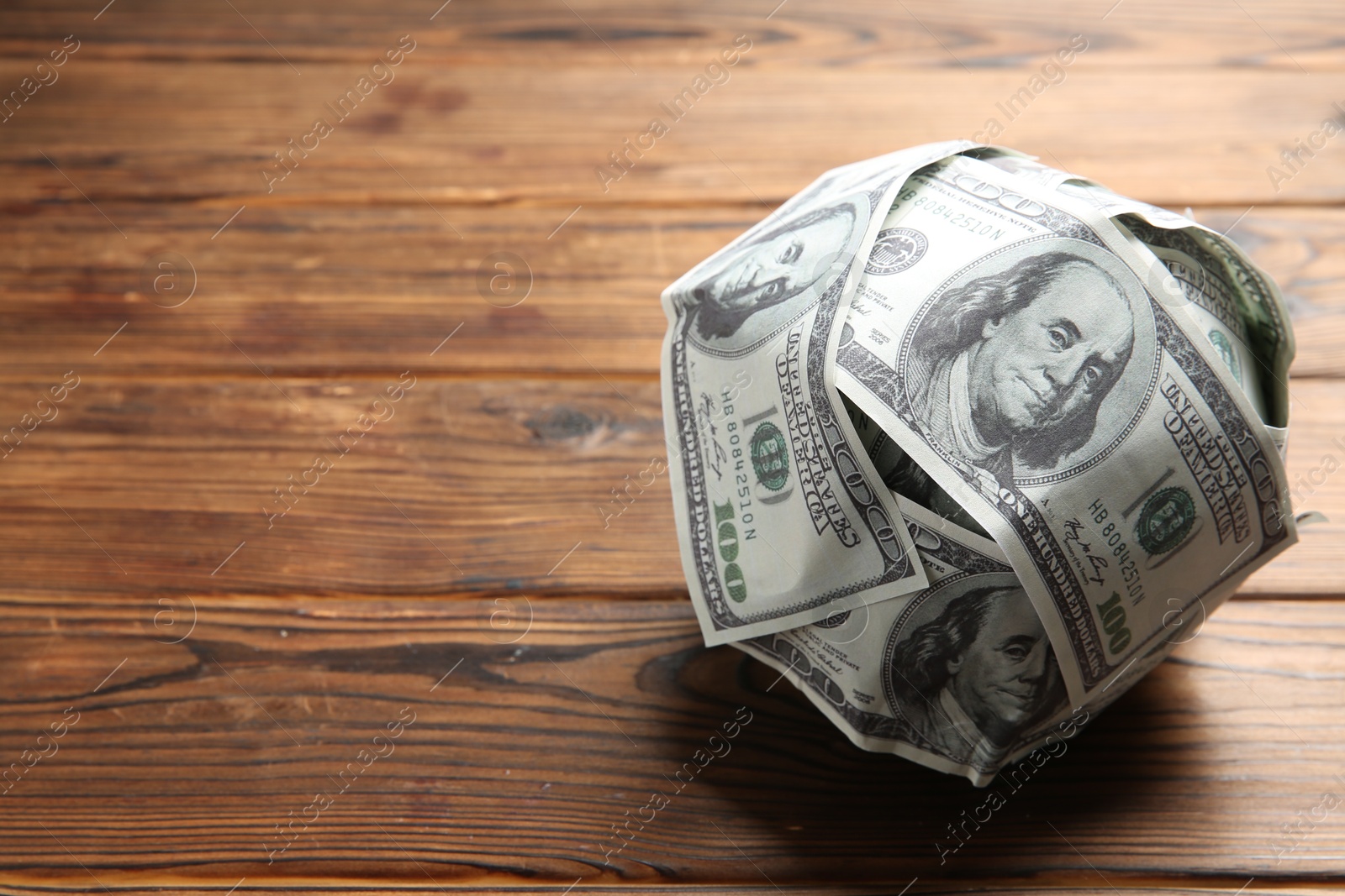 Photo of Ball made of dollars on wooden table. Space for text