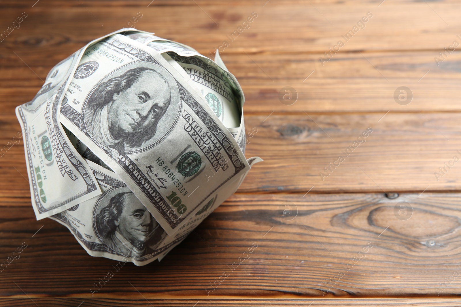 Photo of Ball made of dollars on wooden table. Space for text