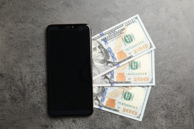 Photo of Modern smartphone and dollar bills on grey table, top view