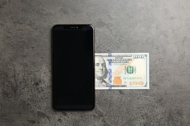 Photo of Modern smartphone and dollar bills on grey table, top view