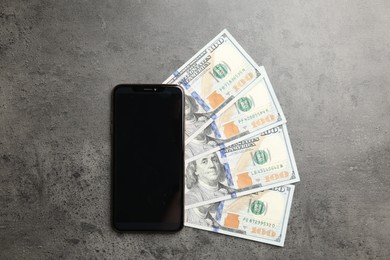 Photo of Modern smartphone and dollar bills on grey table, top view