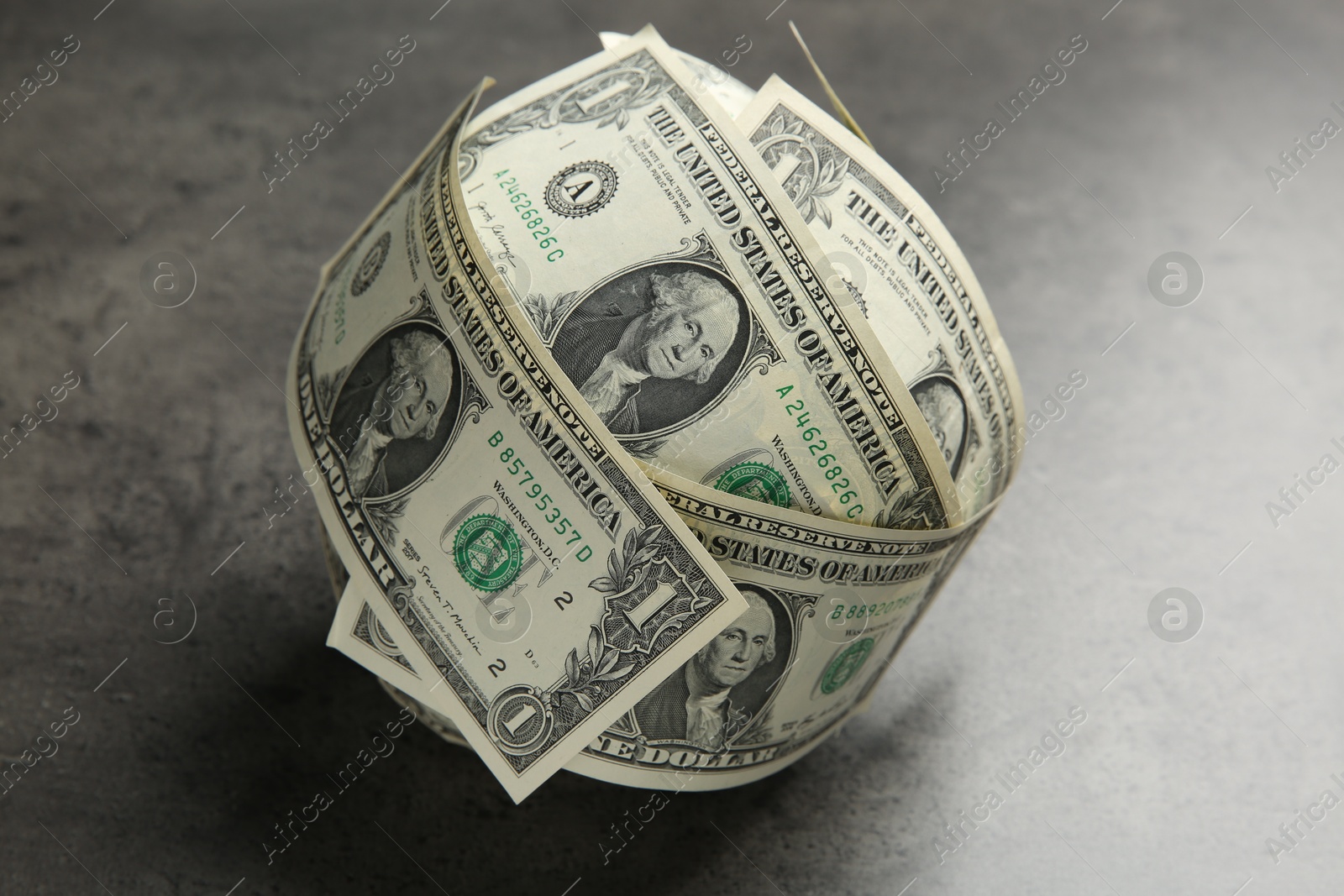 Photo of Ball made of dollars on grey table, closeup