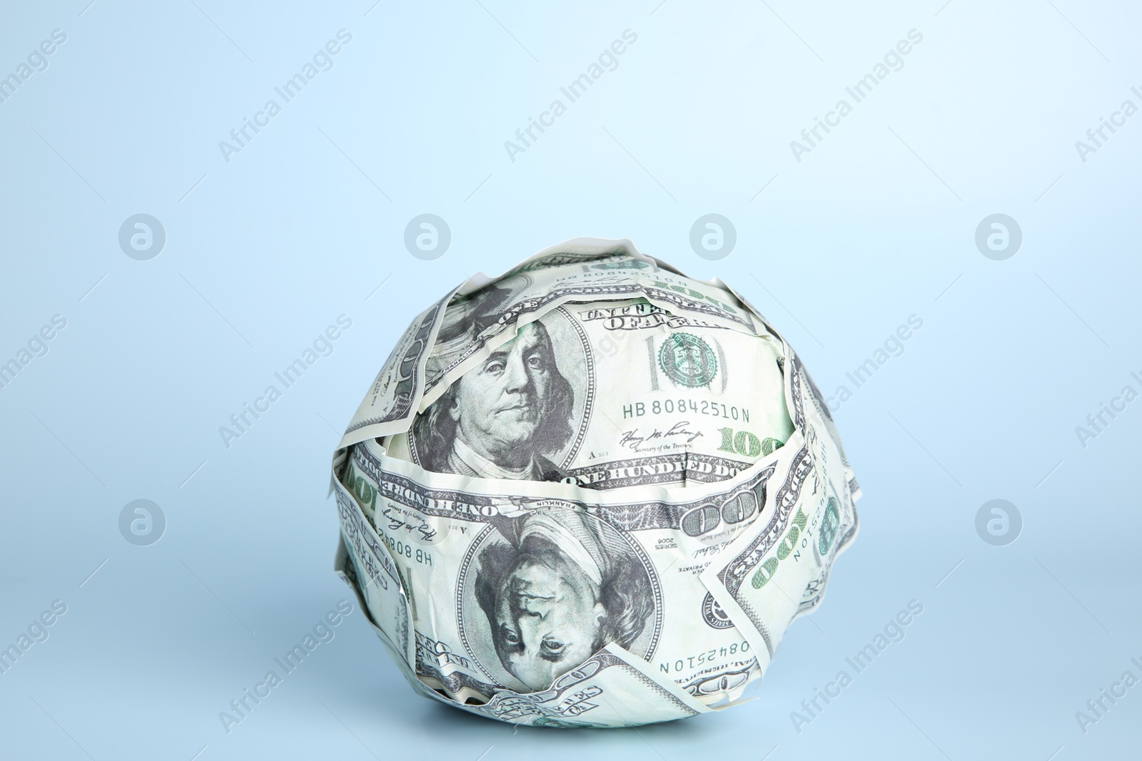 Photo of Ball made of dollars on light blue background